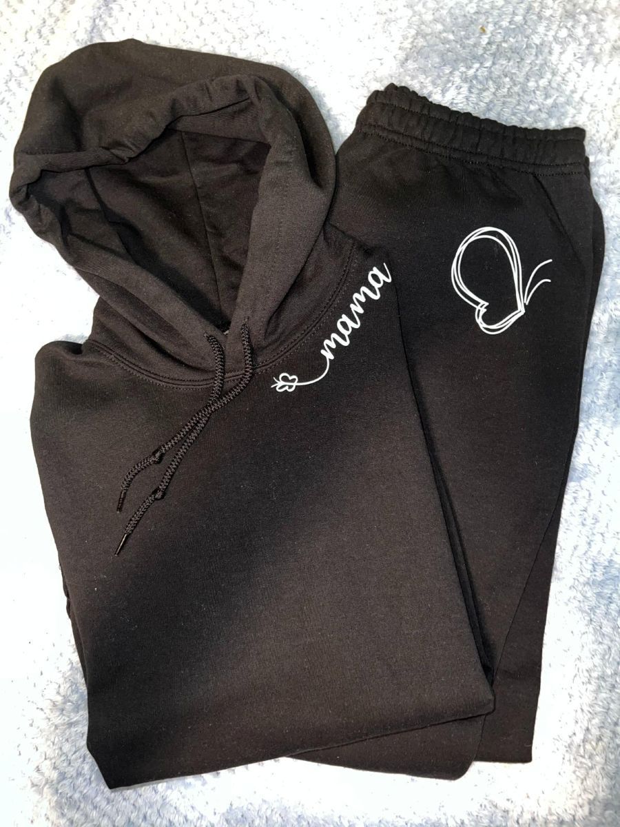 A black hoodie and sweatpants are sitting on a blanket.