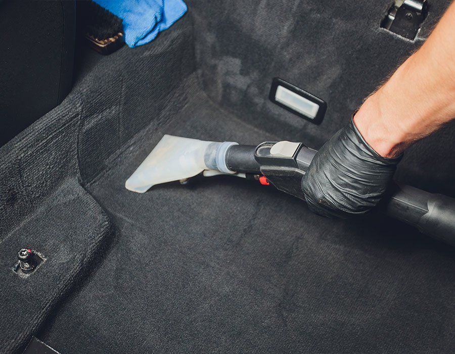 A person is using a vacuum cleaner to clean the carpet in a car.