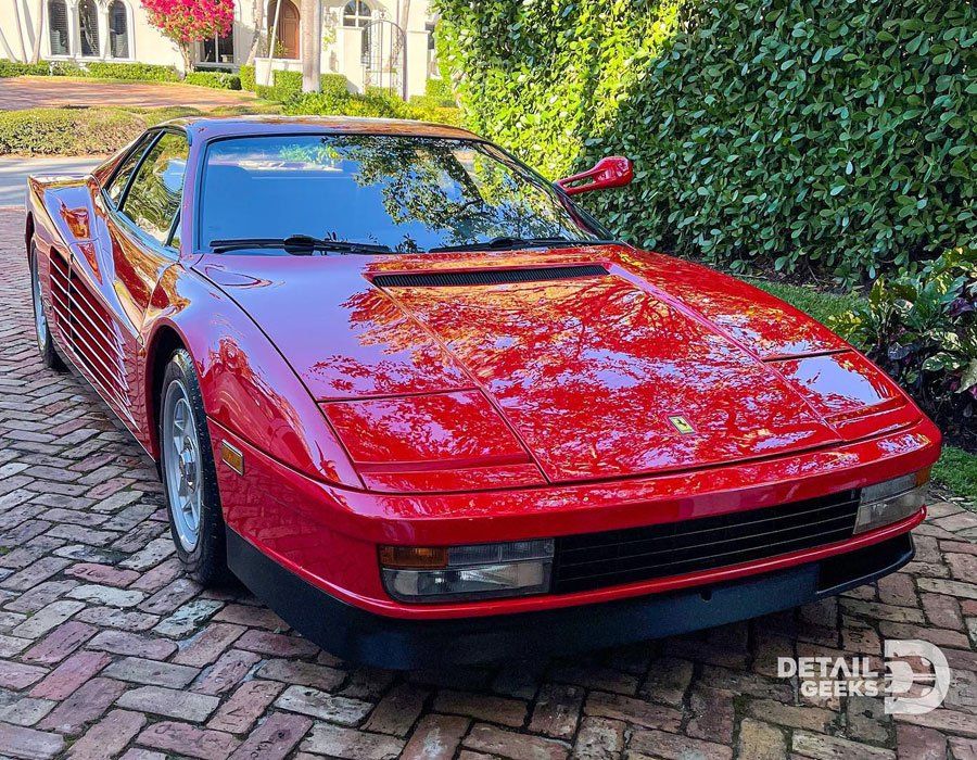 A red ferrari testarossa is parked on a brick driveway.