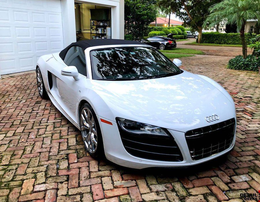 A white audi r8 convertible is parked in front of a garage door.