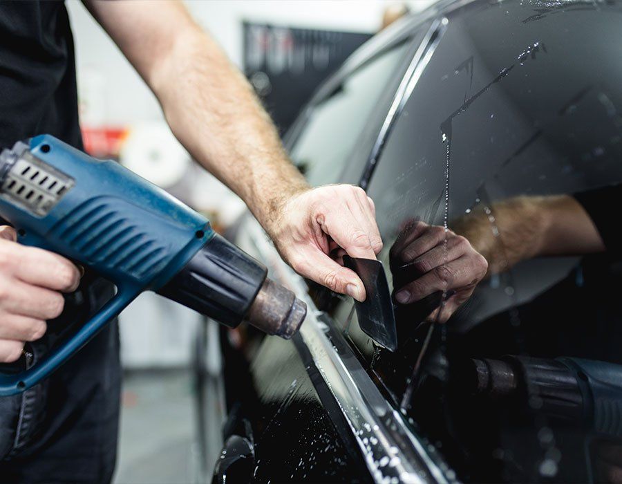Person applying window tint to a car, using a heat gun and squeegee.