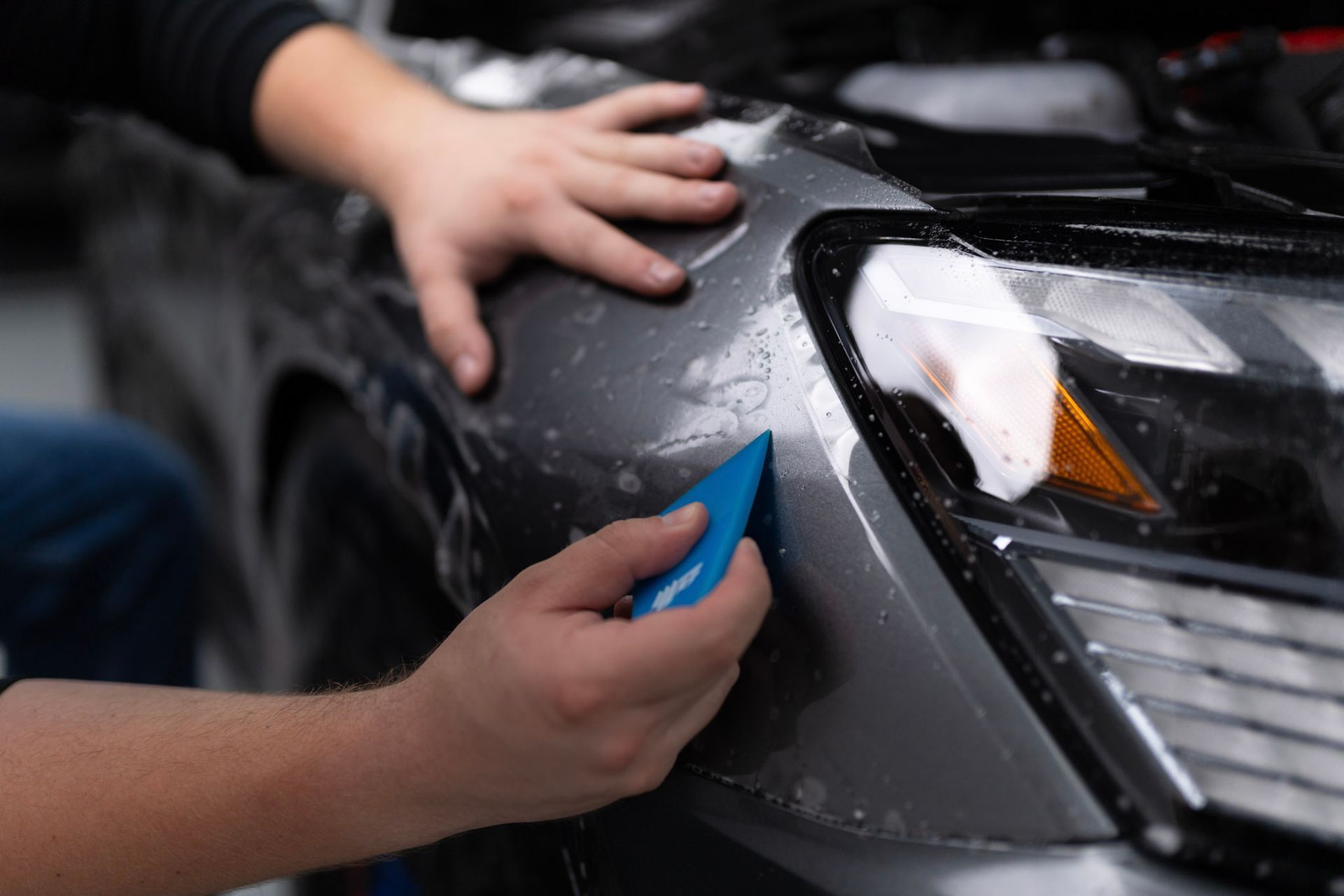 A person is applying protective film to the front of a car.