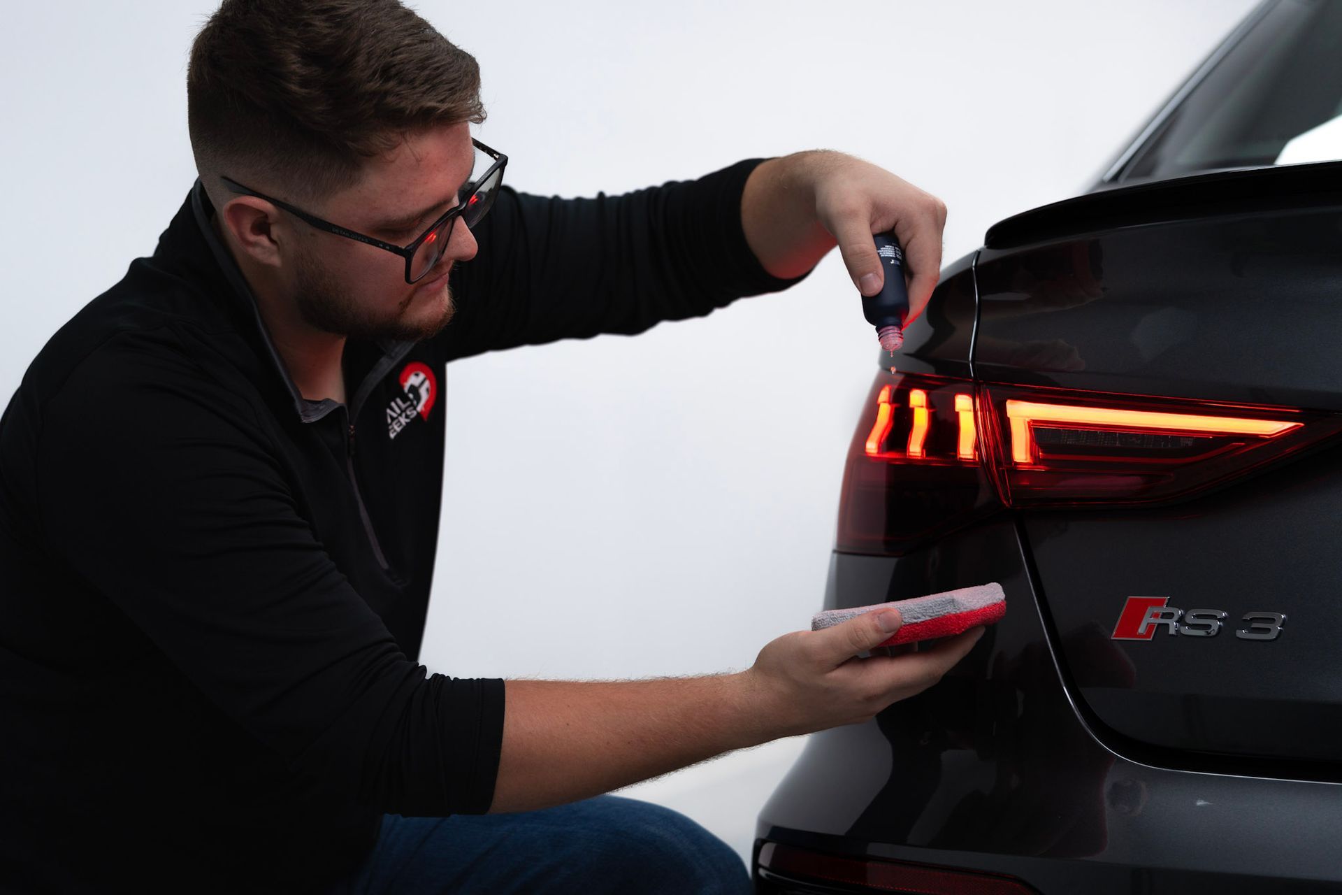 A person wearing blue gloves is polishing the headlight of a white car.