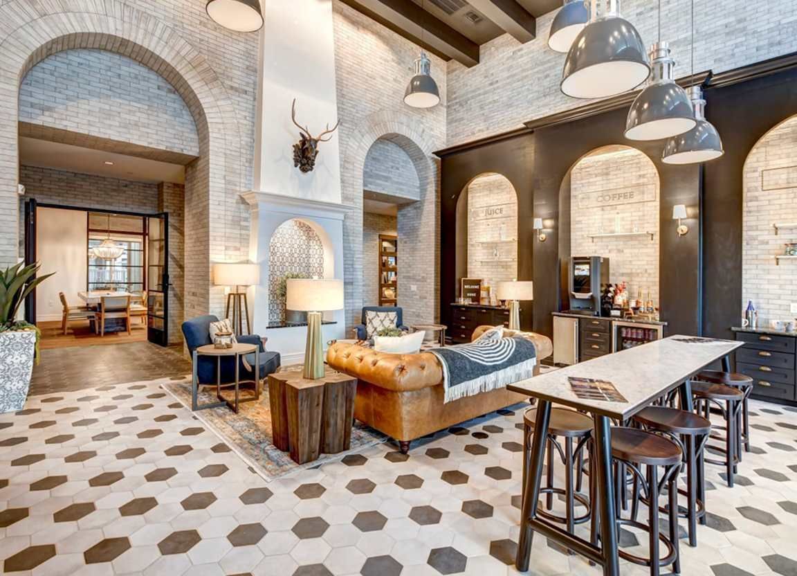 A spacious lounge with brick archways, leather furniture, and a long table with stools. Gray and white patterned floor.