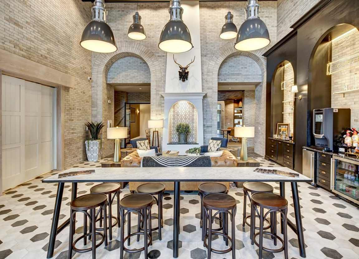 Lounge area with long table and stools, arched doorways, brick walls, pendant lights, and a coffee station.