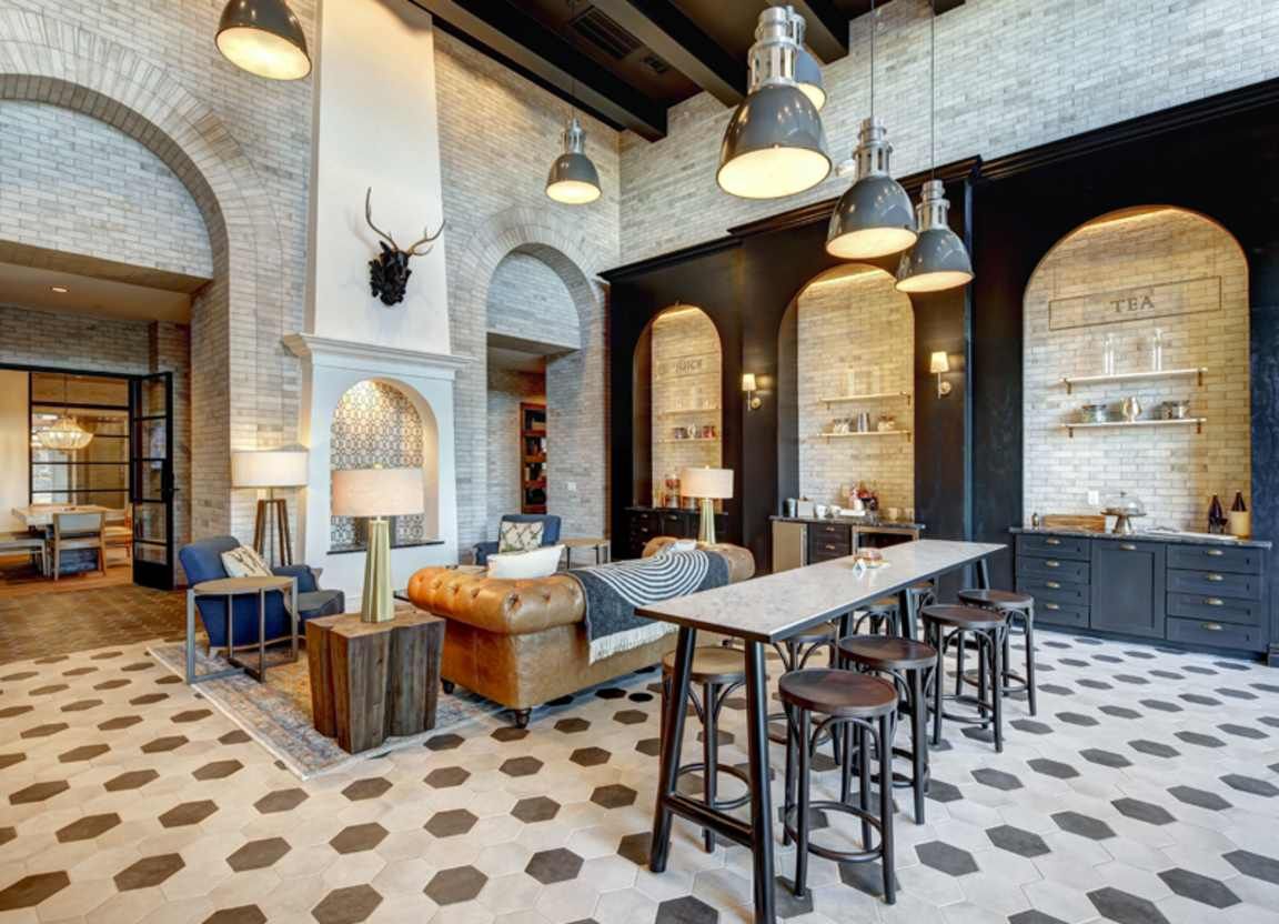 A luxurious lounge area with brick walls, arches, a long table with stools, a leather couch, and pendant lights.