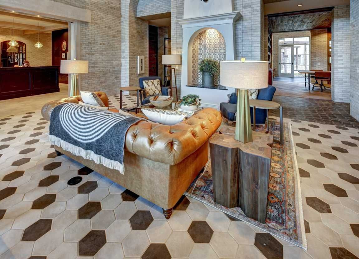 Lobby with a tan leather couch, wooden side tables, and patterned tile floors. It's a welcoming space with a fireplace and front desk.