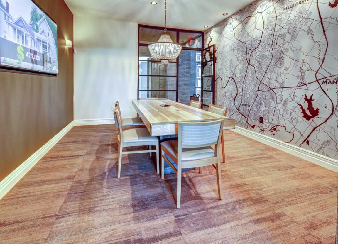 A modern lounge with a wooden table, four chairs, a map-patterned wall, and a chandelier.