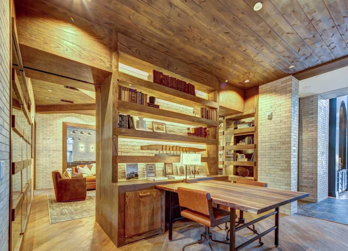 A cozy lounge area wood paneling, a desk, bookshelves, and seating. Warm lighting illuminates the space.