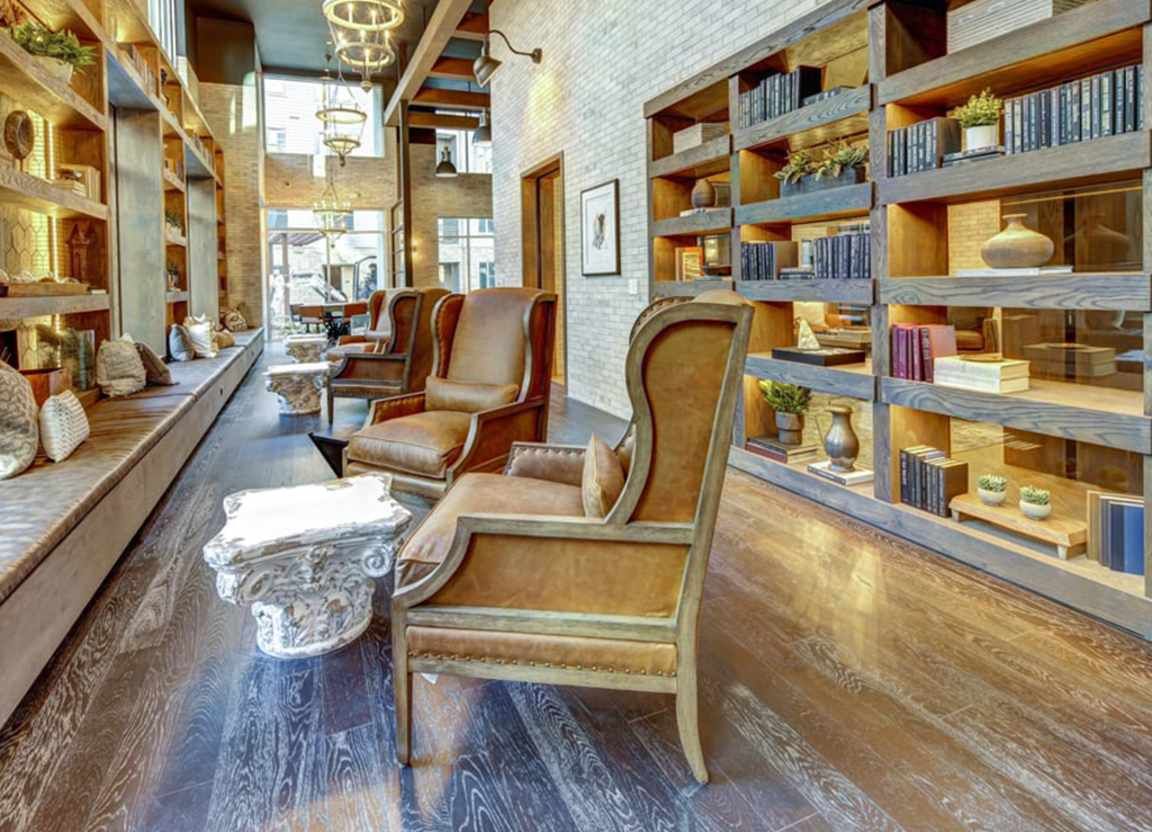 A cozy lounge area with bookshelves, armchairs, and a decorative stone table; wood floors and exposed brick.