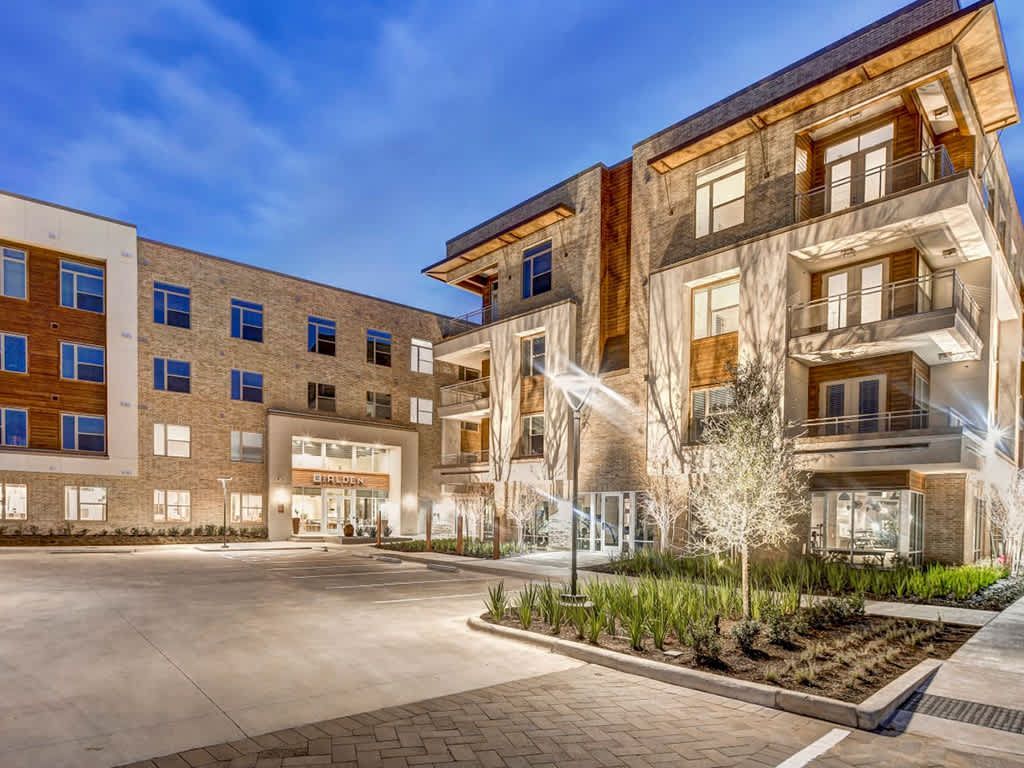Exterior of modern apartment complex with light-colored brick and stone, illuminated at dusk.