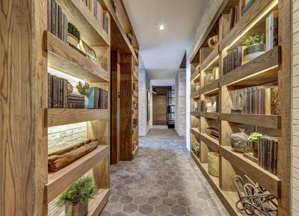A hallway with wooden bookshelves on both sides, lit by warm lights. The shelves hold books and decorative items.