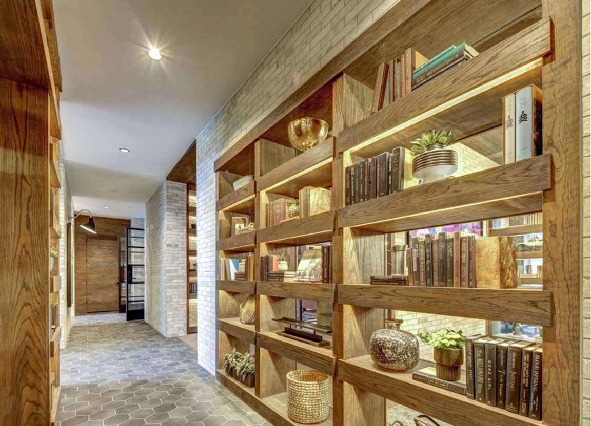 Hallway with built-in wooden bookshelves filled with books and decorative items; white brick wall on the left.