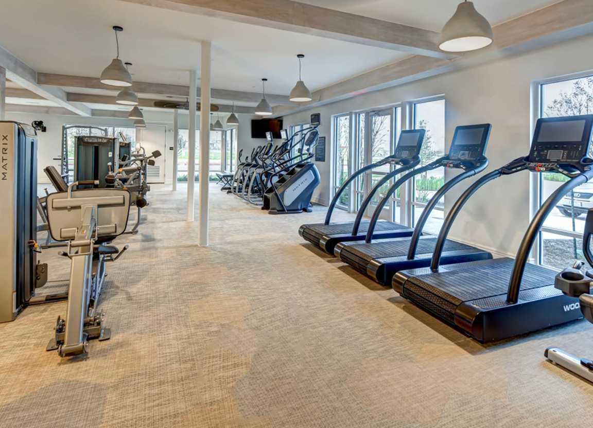 Spacious gym with cardio machines and weight equipment, neutral tones, and bright lighting.