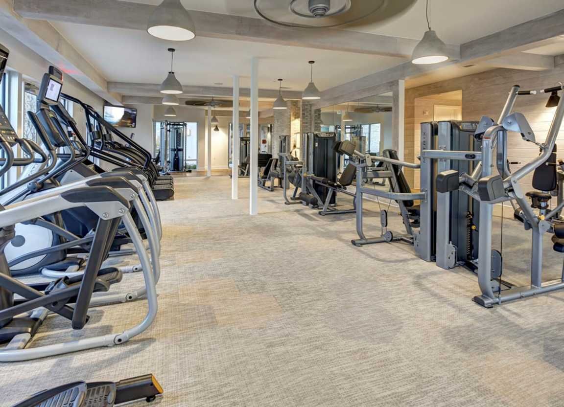Gym with cardio machines and weight machines, mostly gray and silver, with a light gray carpet.