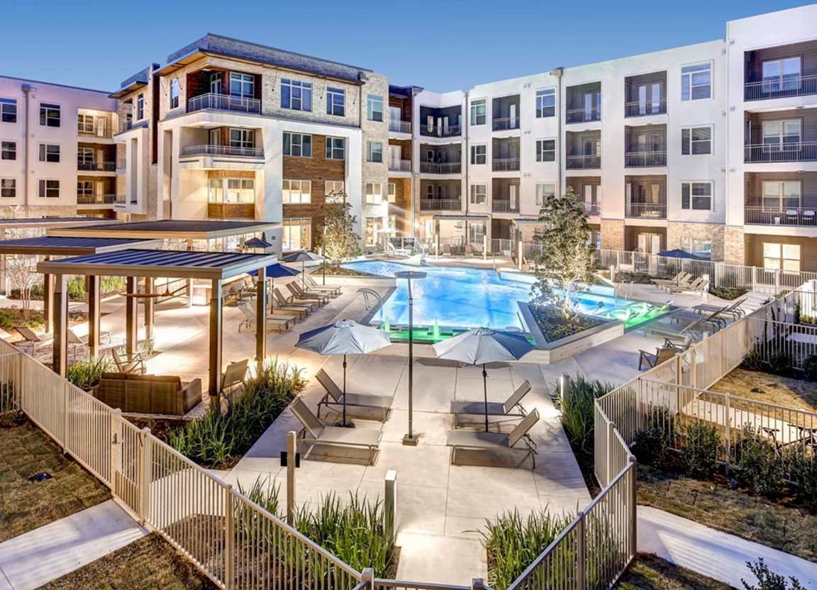 Apartment complex courtyard with a pool, lounge chairs, and a pergola. Buildings surround the courtyard.