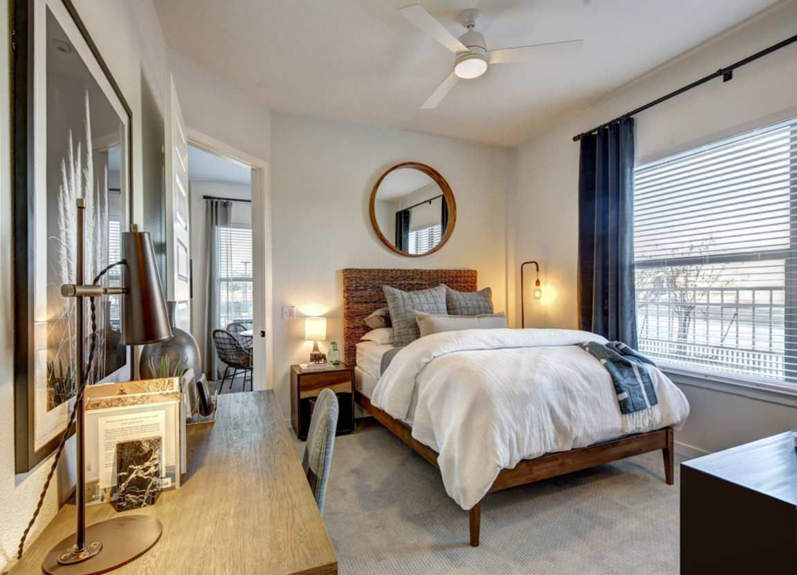 Bedroom with a wooden bed, desk, and round mirror. Neutral colors with pops of blue.