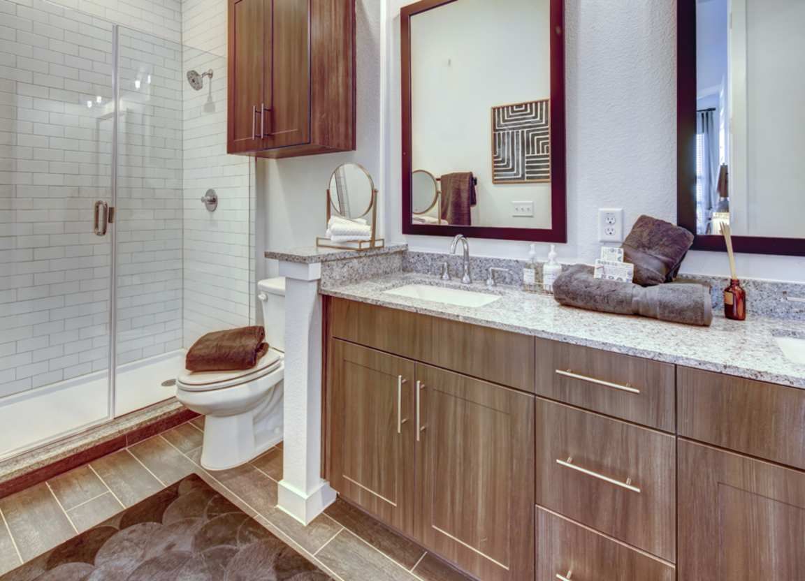 Bathroom with a glass-walled shower, a vanity with a marble countertop, a toilet, and a dark wood cabinet.