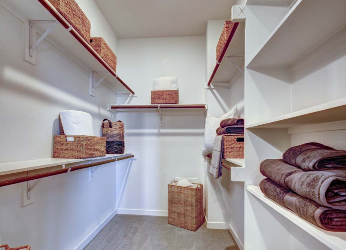Walk-in closet with white shelves and wicker baskets holding towels and linens. Light-colored flooring and walls.