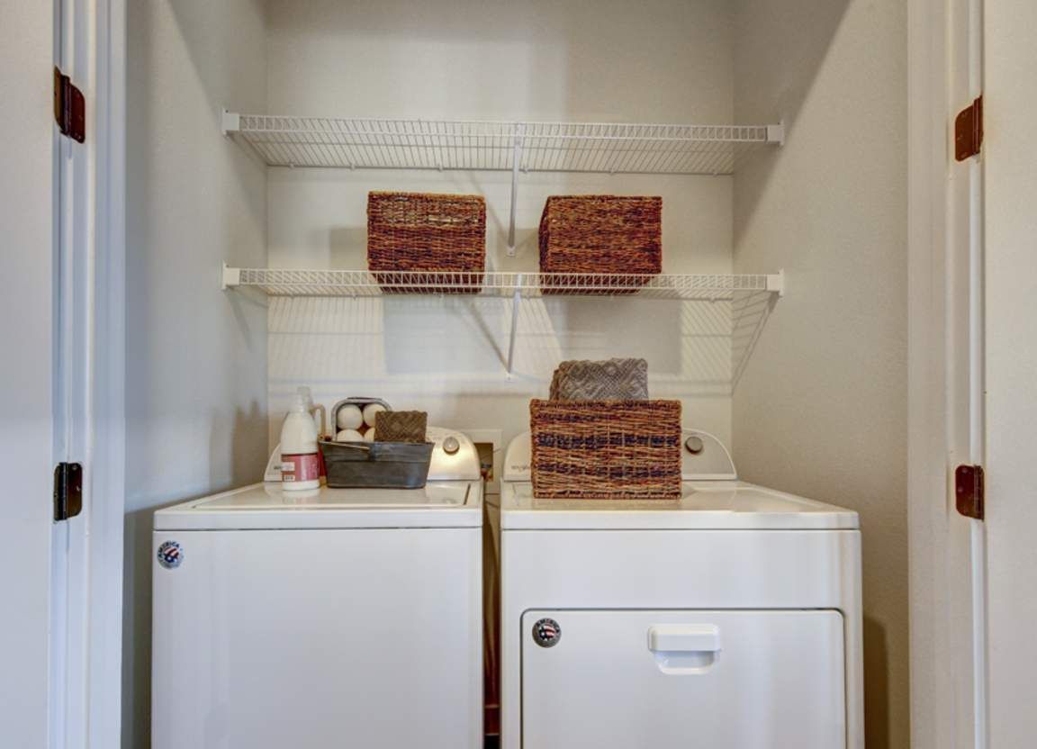 Laundry room with a white washer and dryer, shelves with baskets and supplies.