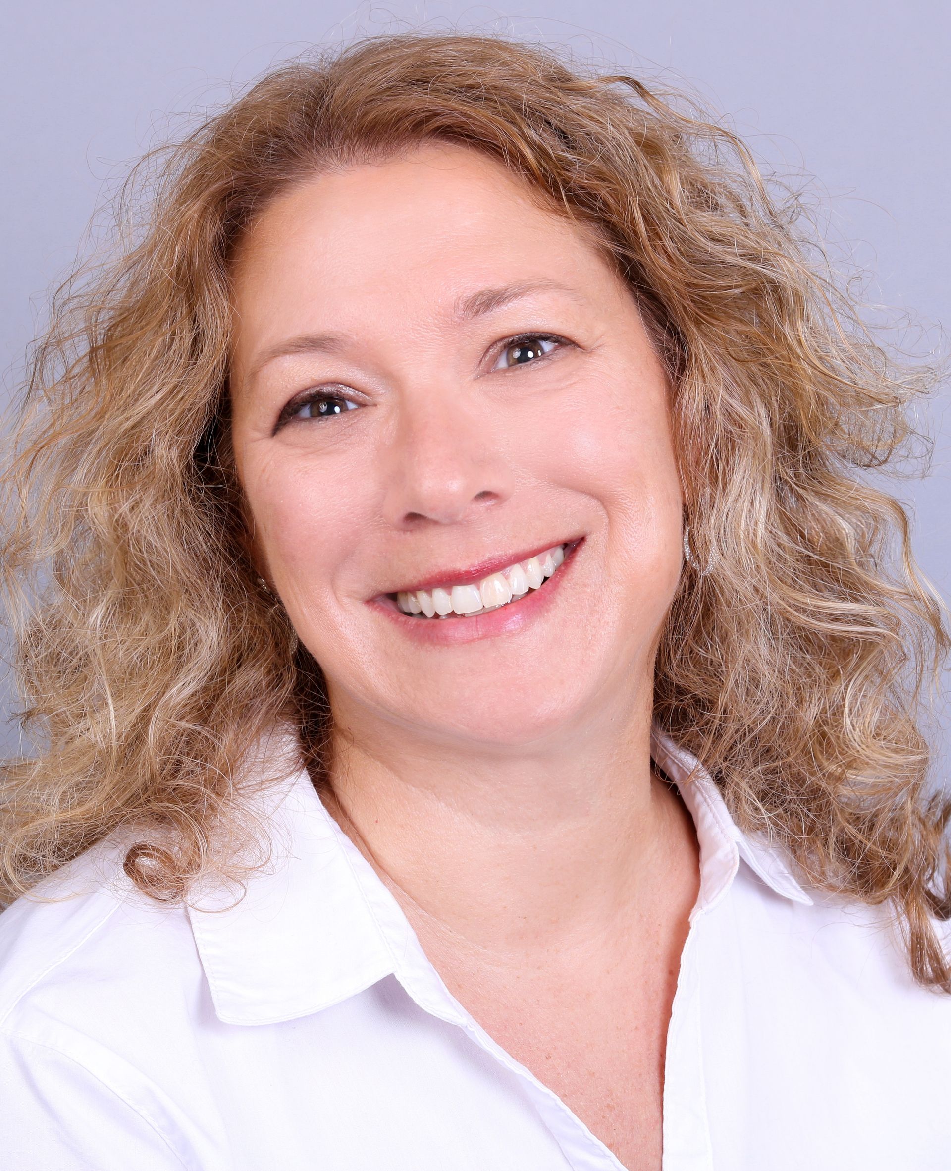 Woman with curly blonde hair smiling broadly in a white shirt against a blue background.