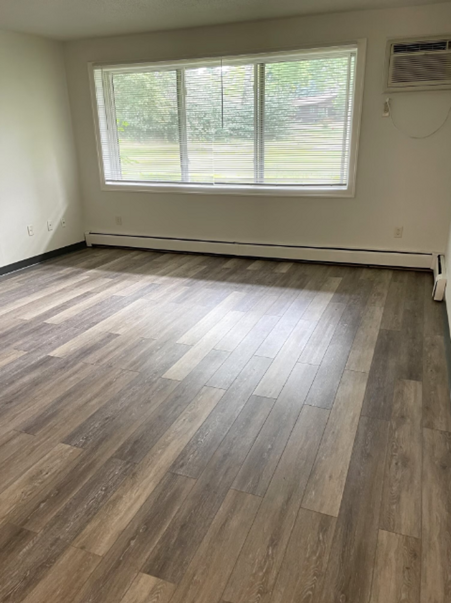 An empty living room with hardwood floors and a large window.