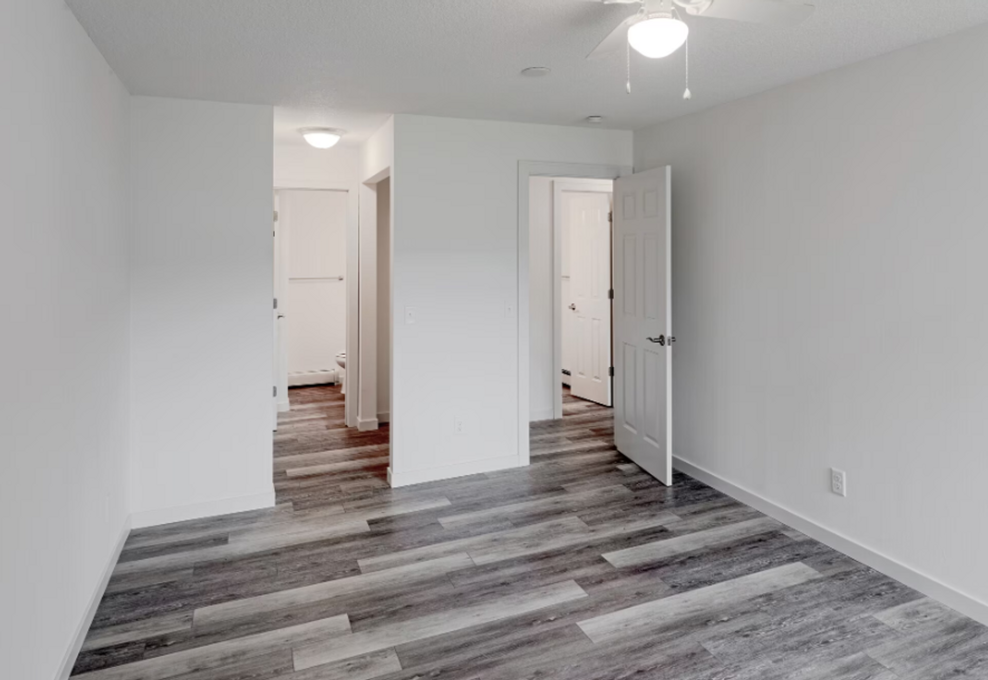 An empty bedroom with hardwood floors and a ceiling fan.