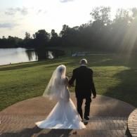 Bride and groom walking on a path beside a lake at sunset
