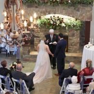 Wedding ceremony under floral arch in rustic stone venue, bride and groom standing with officiant