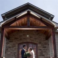 Bride and groom kissing beneath a wooden porch in front of a stone house
