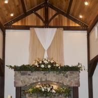 Decorated church altar with white drapery, greenery, and white flowers under a wooden vaulted ceiling