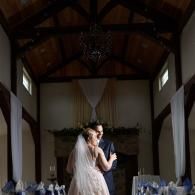 Bride and groom slow dance in a rustic hall with high wooden beams and soft window light