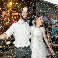Newlyweds smiling under falling confetti outside a building