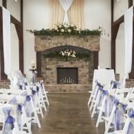 Decorated wedding ceremony hall with white chairs, blue ribbons, and a stone fireplace altar