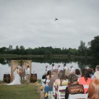 Outdoor wedding ceremony by a lake, with guests seated facing an altar under a cloudy sky.