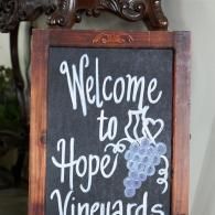 Welcome sign for Hope Vineyards on a black chalkboard with a white grape drawing