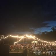 Outdoor evening wedding reception under string lights with tables and guests under a dark sky