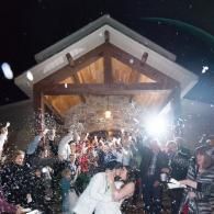 Wedding celebration under a wooden pavilion, with guests dancing and tossing confetti at night