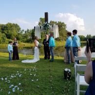 Outdoor wedding ceremony with bride and groom under a white arch on a grassy lawn