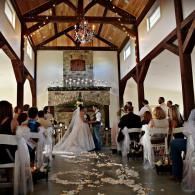 Bride and groom at altar in a rustic church, guests seated on either side, flower petals on the aisle