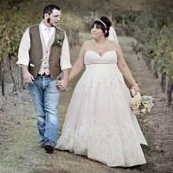 Wedding couple walking hand in hand outdoors; bride in white gown, groom in vest and jeans.