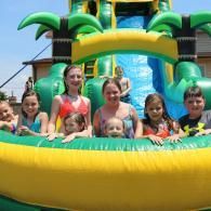Children posing in a yellow inflatable water slide pool with palm-tree decorations at a water park