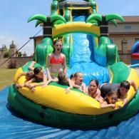 Children on a colorful inflatable water slide, splashing and smiling outdoors.