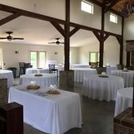Empty banquet hall with round and rectangular tables draped in white linens and dark wooden beams overhead