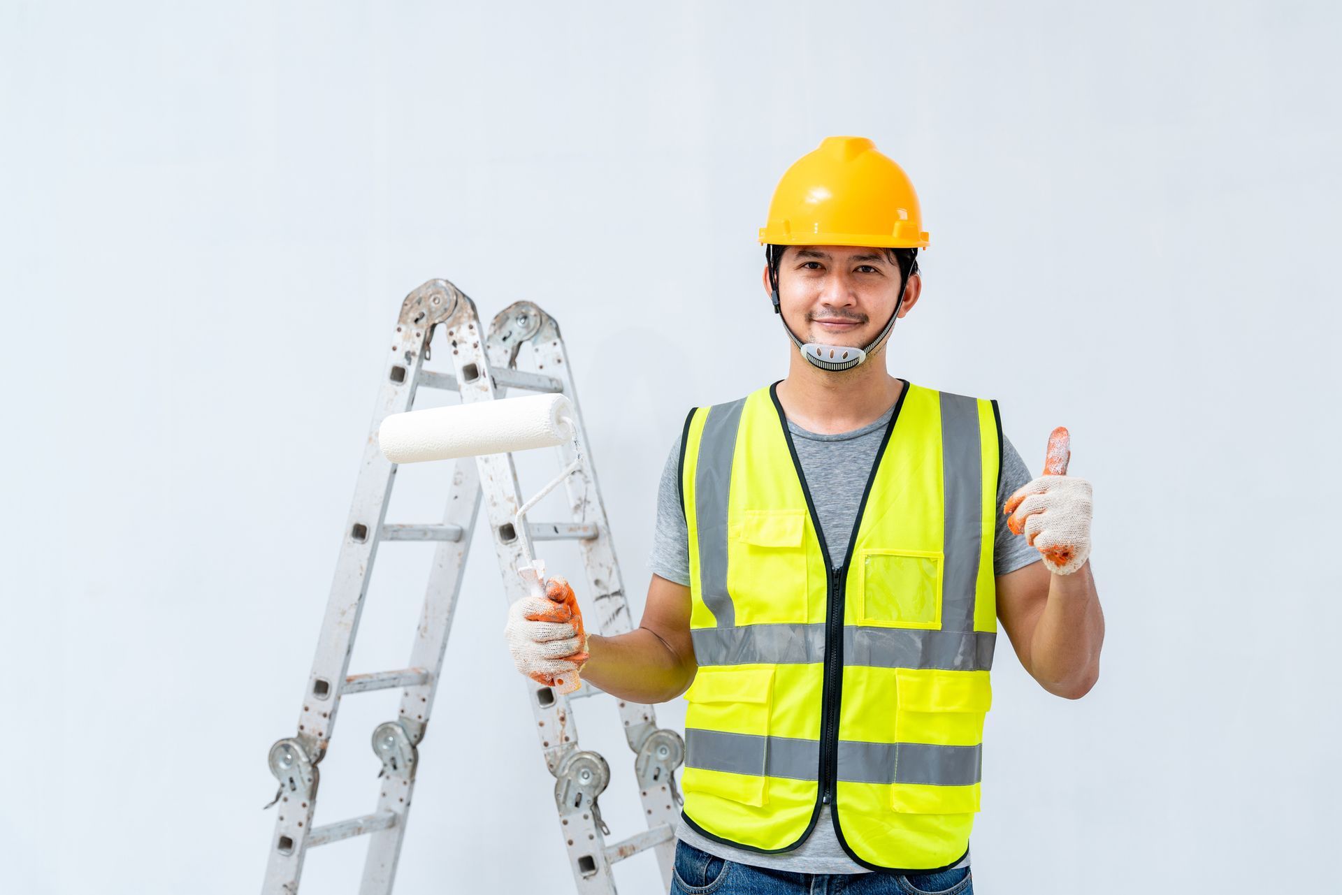 A construction worker is holding a paint roller and giving a thumbs up.