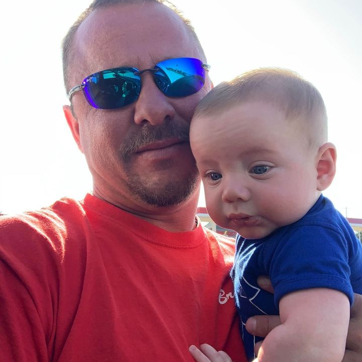 A man wearing sunglasses is holding a baby