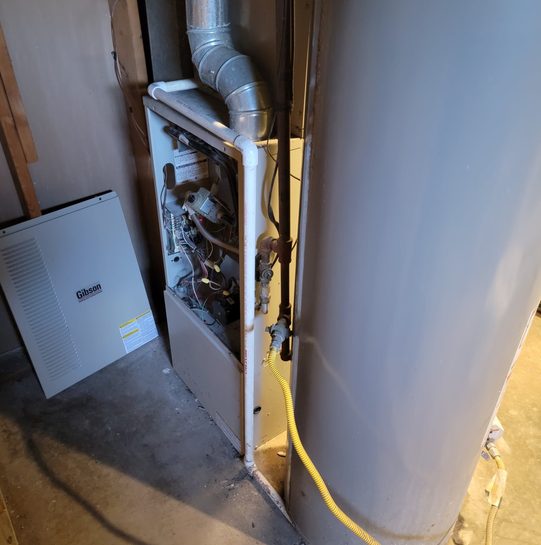 A gas heater is sitting next to a water heater in a basement.