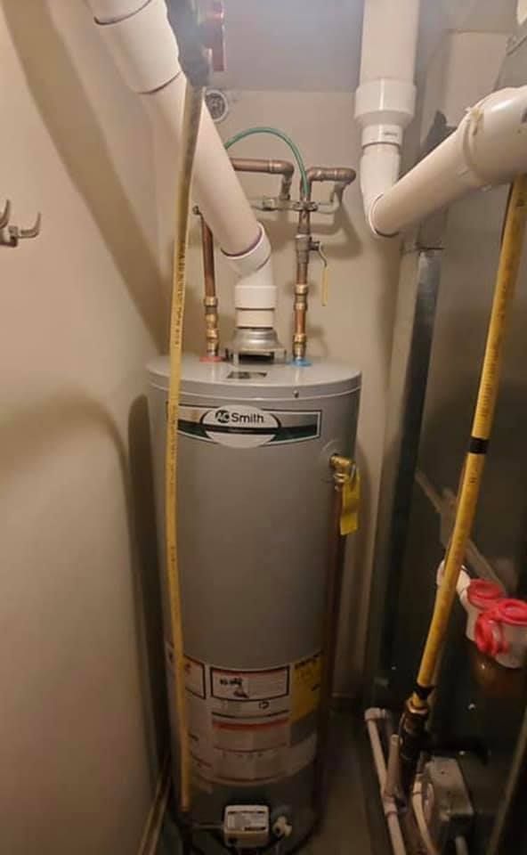 A water heater is sitting in a room next to pipes.