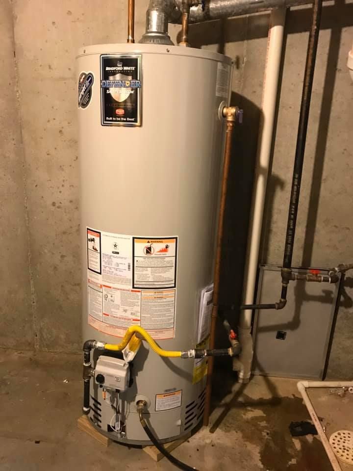 A gas water heater is sitting in a basement next to pipes.