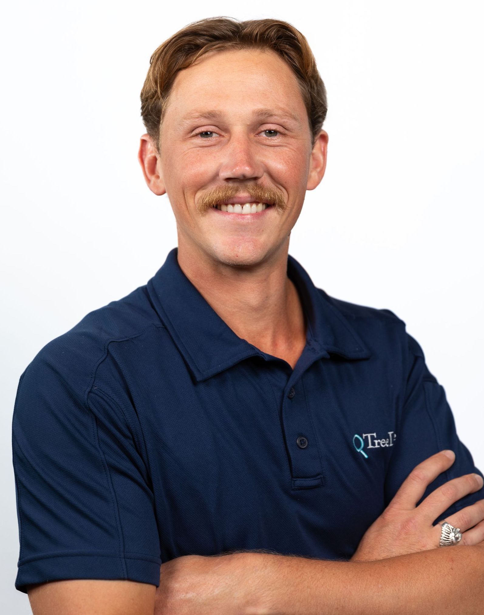 A TreeLife professional wearing a blue polo shirt and a watch is standing with his arms crossed.